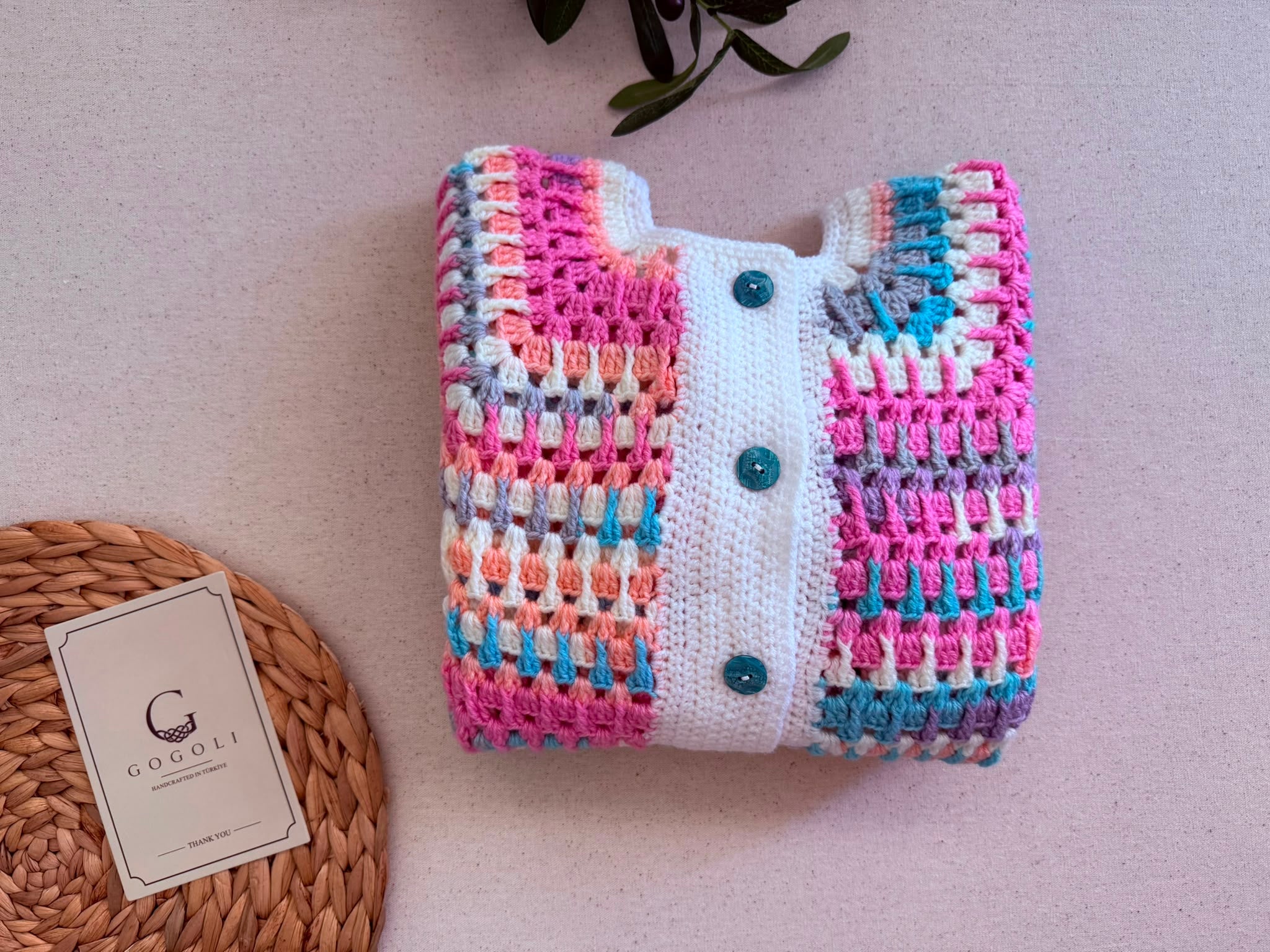 Close folded view of the multicolour crochet cardigan showing the round neckline, white front placket and contrasting dark buttons.