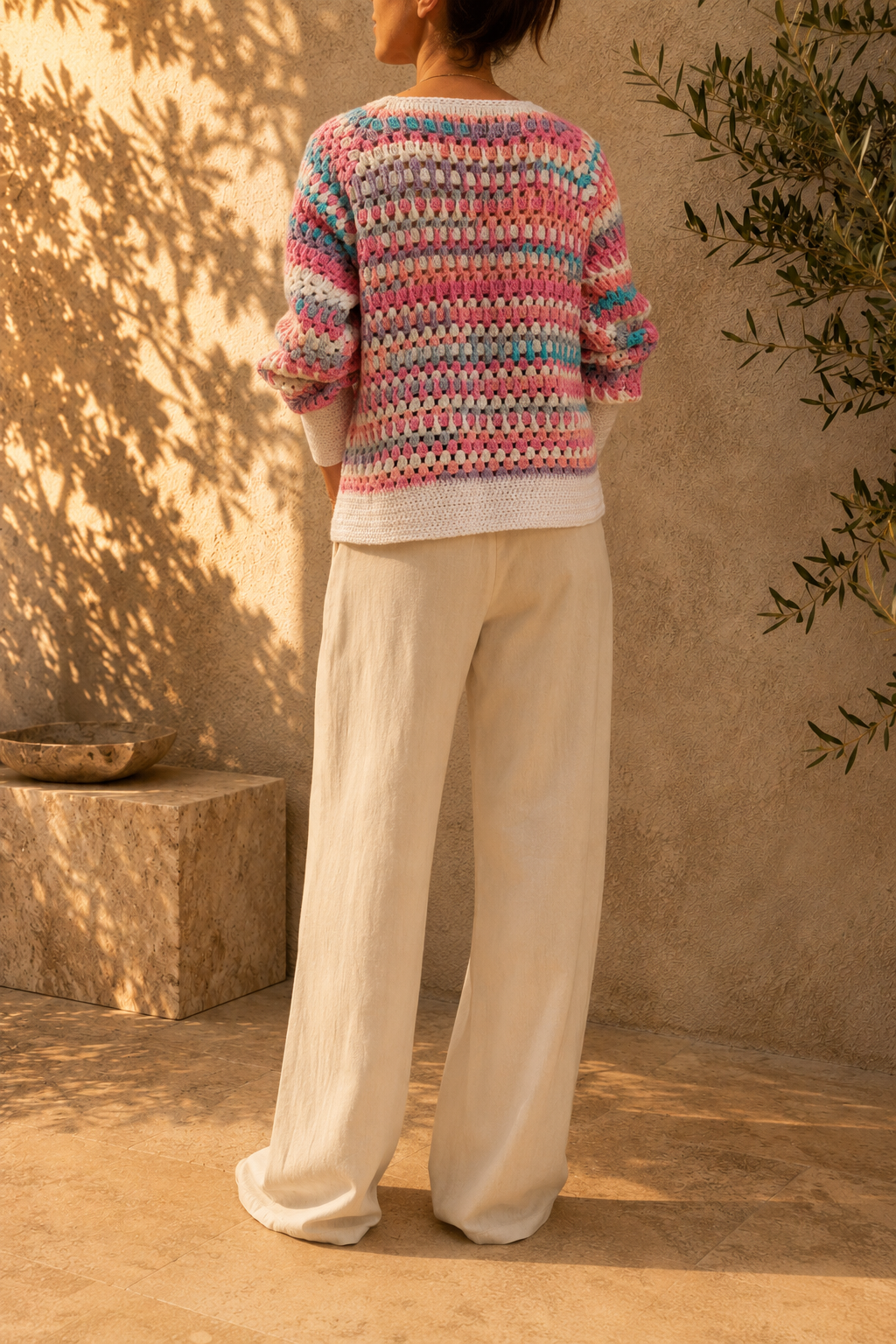 Back view of the multicolour crochet cardigan showing the repeating coloured stripes across the body and long sleeves.