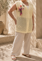 Handmade cream crochet vest styled with light trousers, showing its longline fit and functional pearl-look buttons.