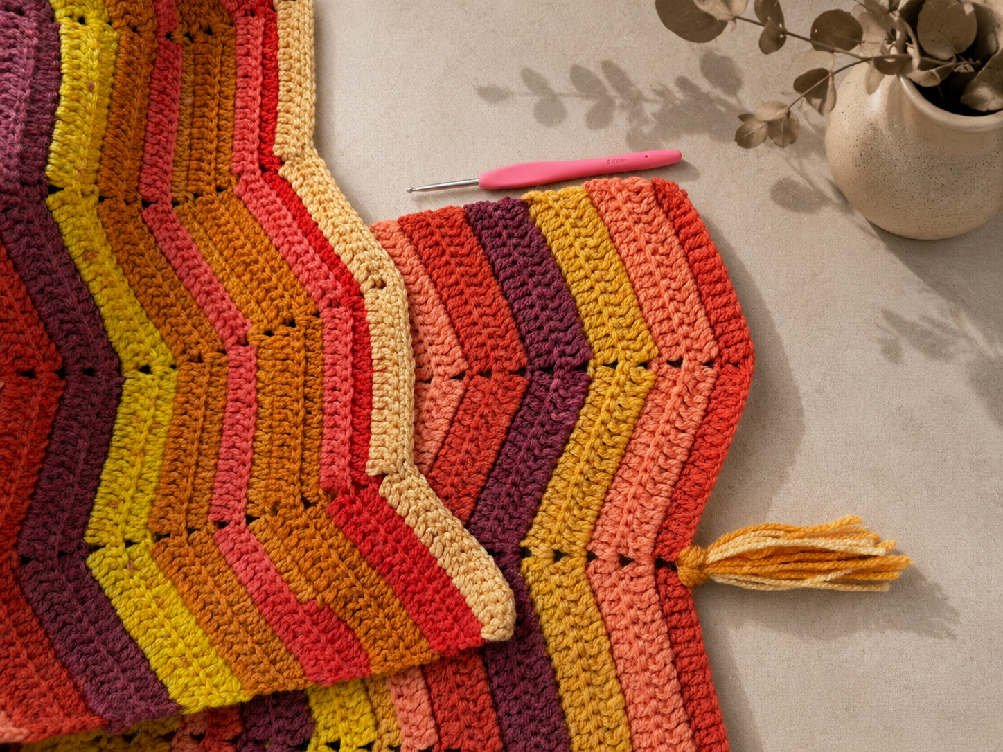Close view of the multicolour chevron crochet blanket laid flat, showing its zigzag edge, stitches and tassel detail.