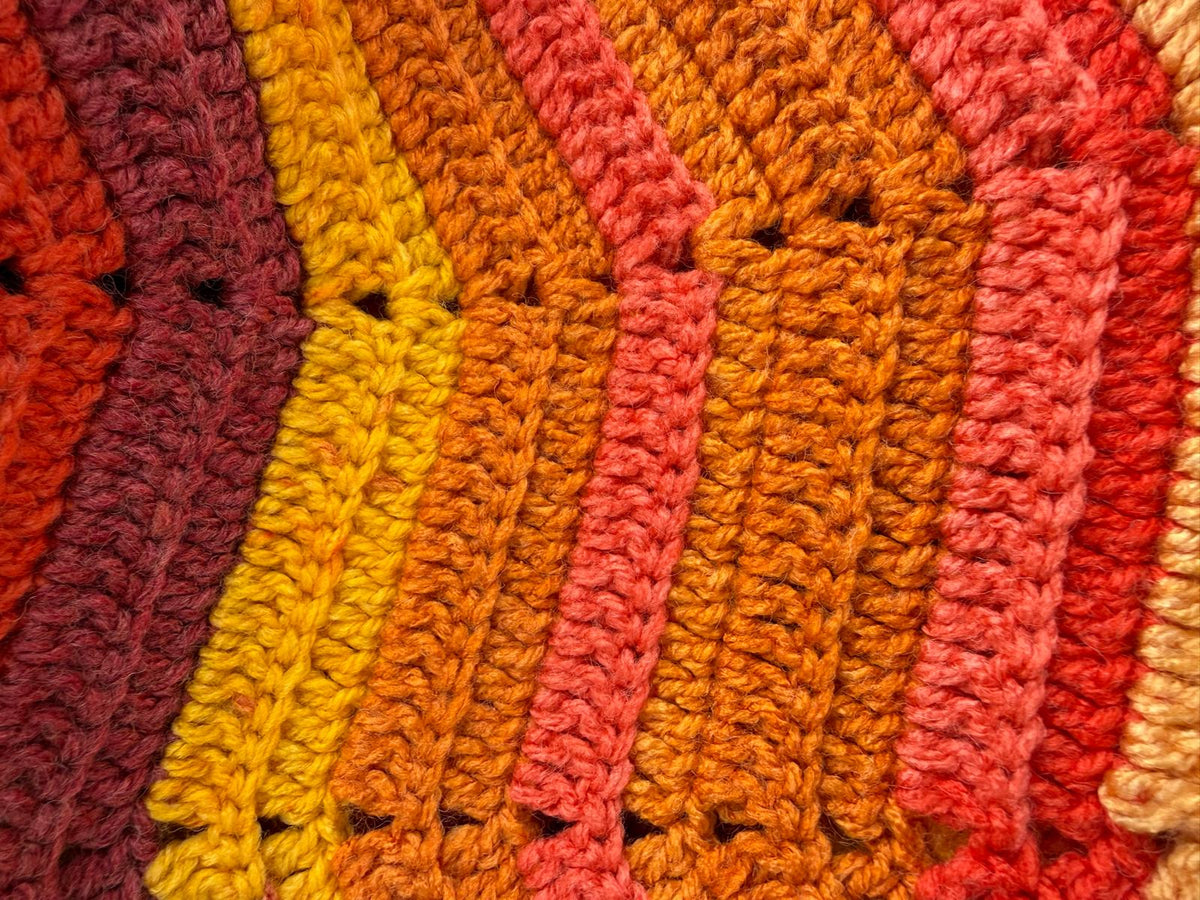 Macro view of the crochet stitches and variegated orange, red, pink and golden colour transitions.