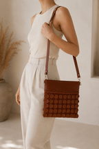 Cognac brown leather sequin crossbody bag worn with a neutral outfit, showing its proportions and long shoulder strap.