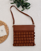 Studio flat-lay of the cognac brown crossbody bag showing the leather top panel, repeated leather sequin rows and long strap.