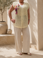 Front view of the handmade cream crochet vest with pearl-look buttons and hand-sewn floral appliqués on one shoulder.