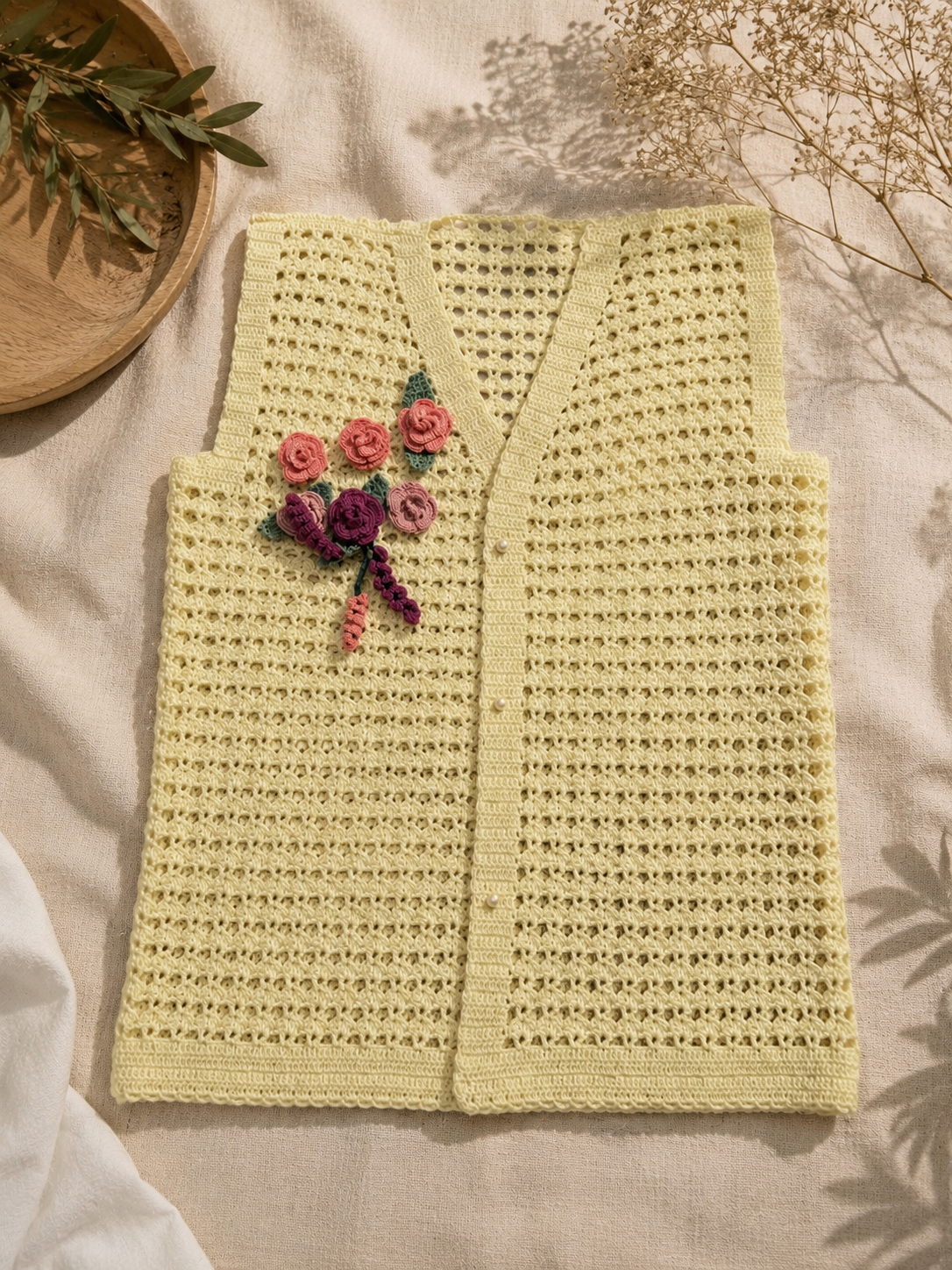 Flat-lay view of the cream crochet vest showing its straight construction, openwork body, floral appliqués and buttoned front.