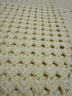 Macro view of the cream openwork crochet texture with a pearl-look plastic button and softly lustrous microfiber acrylic yarn.