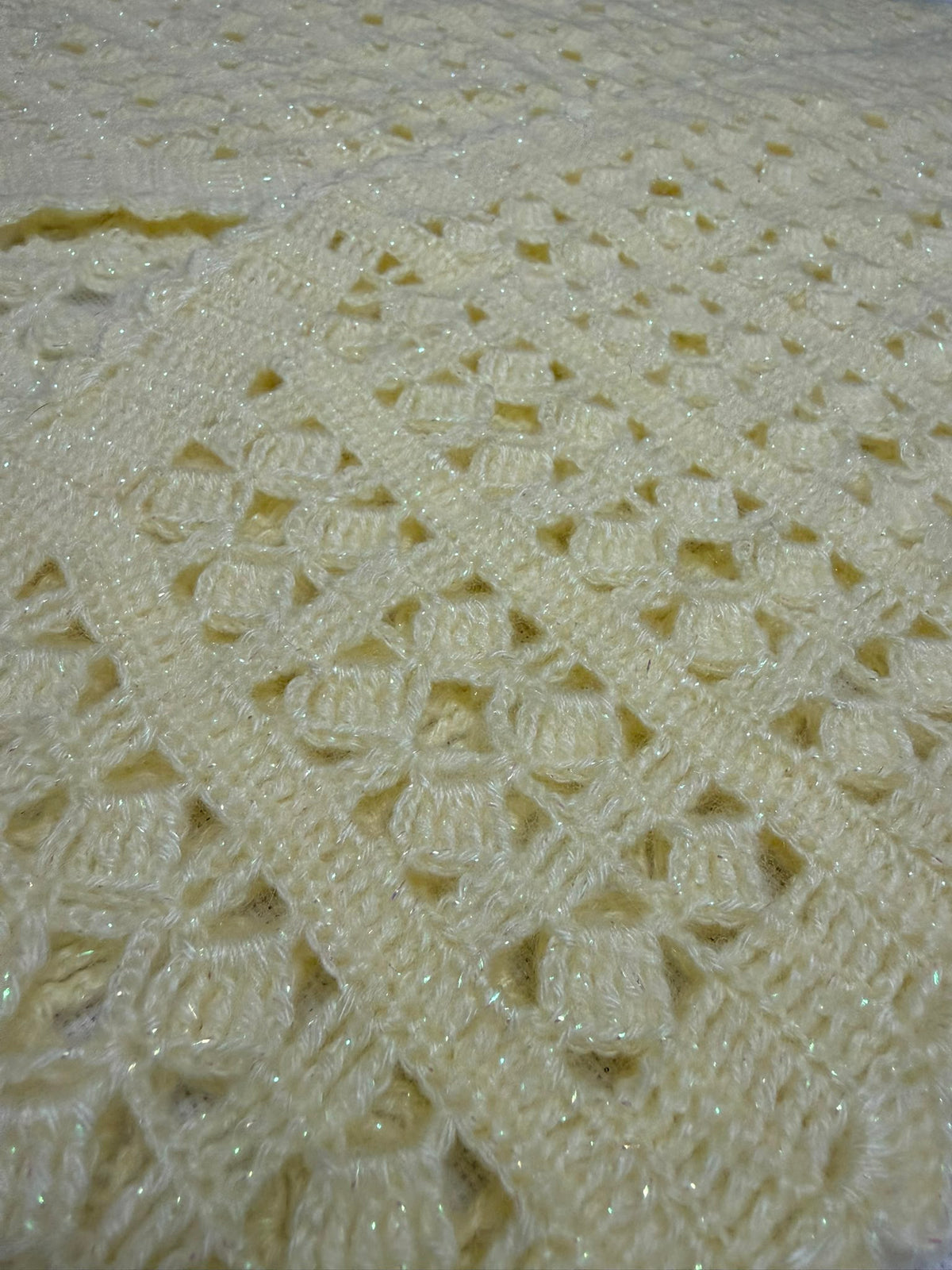 Close-up of the cream crochet vest showing its openwork panel construction and softly defined stitch pattern.