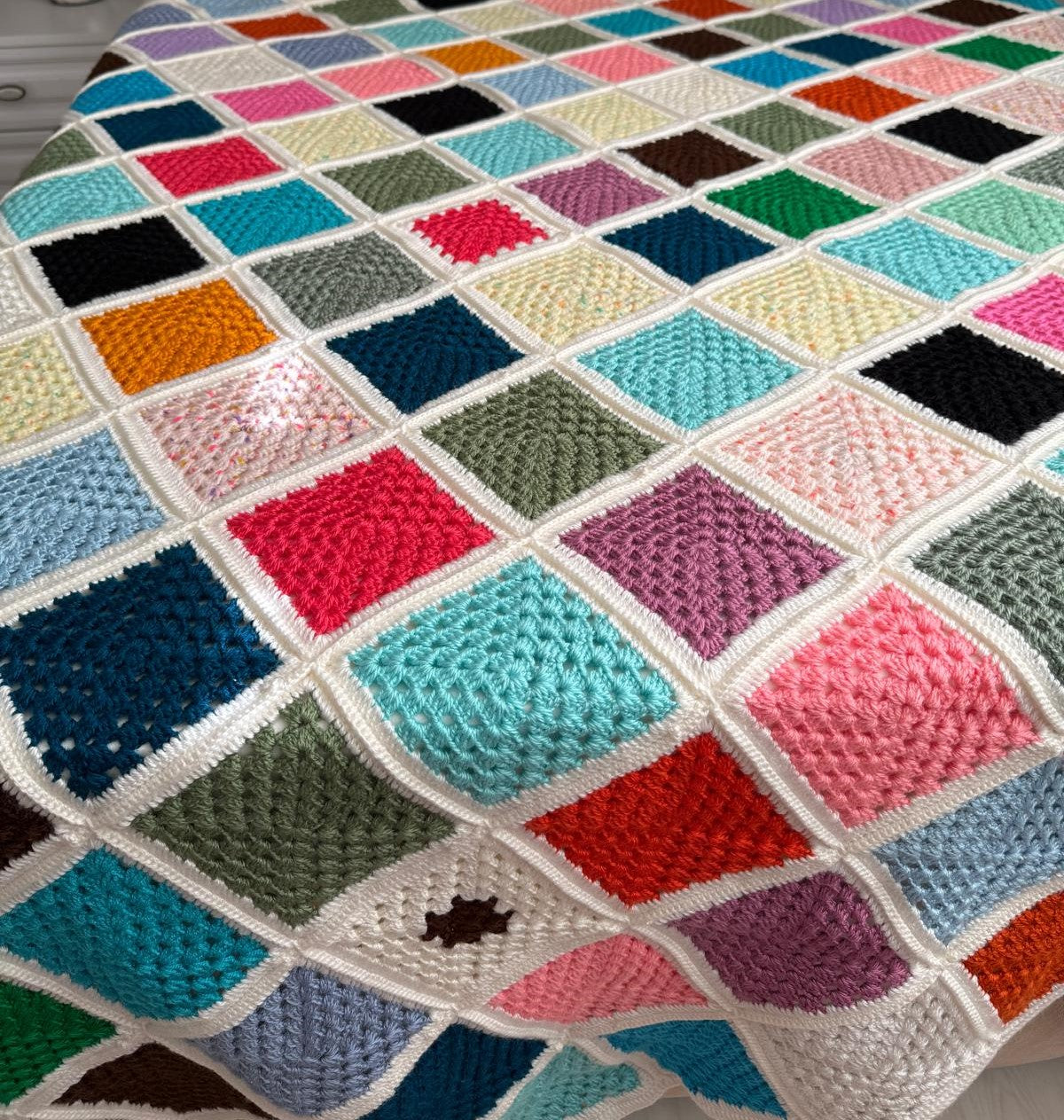 Close-up of the colourful square crochet motifs and hand-joined cream borders of the blanket.