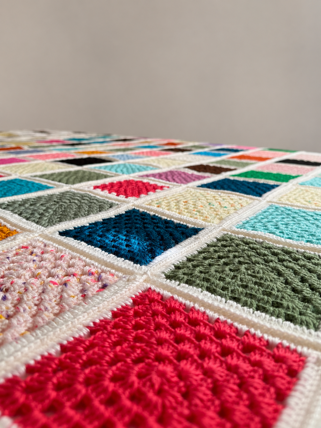 Macro view of the handmade crochet stitches, textured motifs and joining lines in the multicolour blanket.