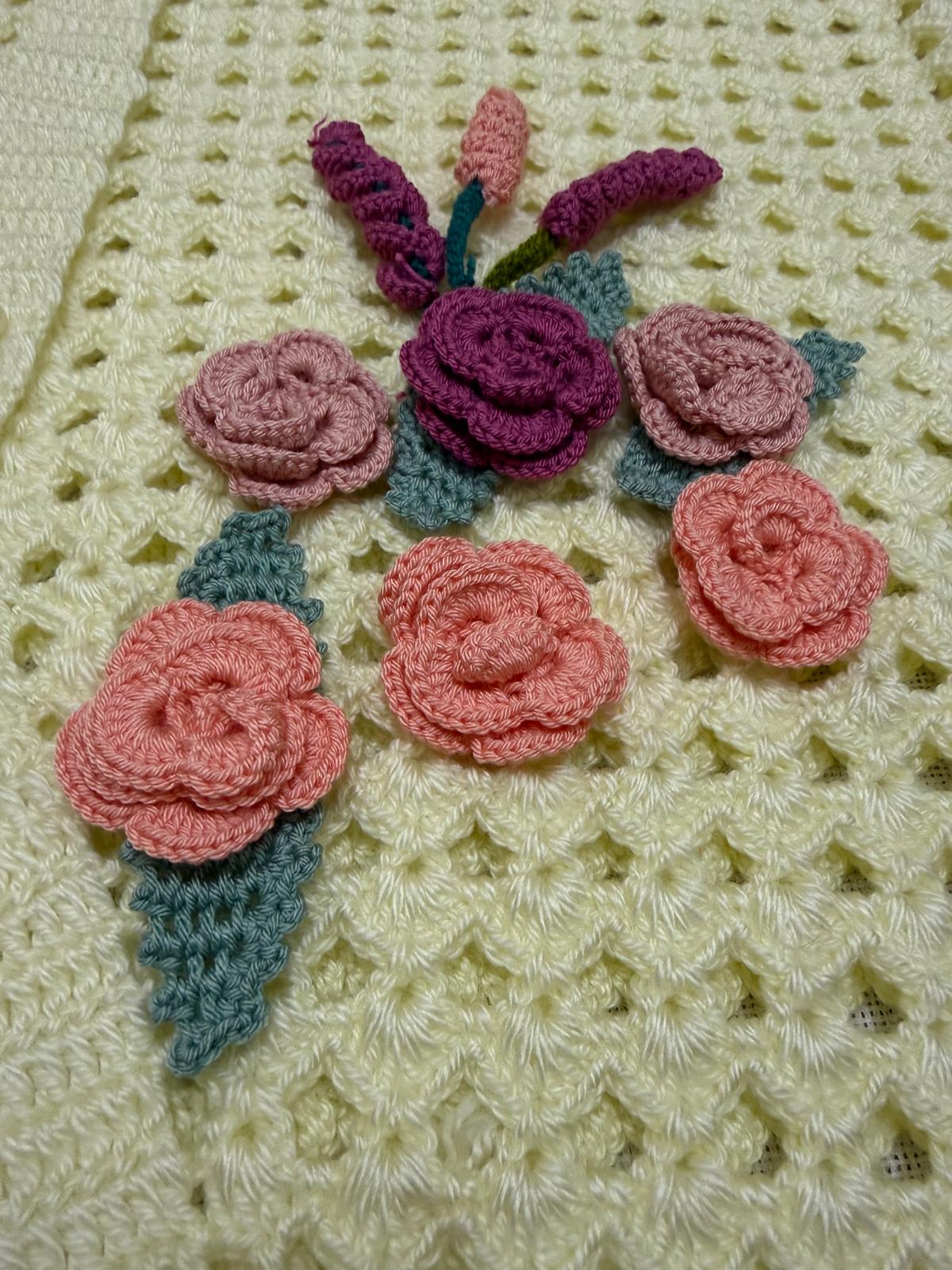 Close-up of the hand-arranged crochet flower and leaf composition in blush, coral, plum and green tones