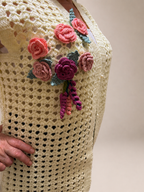 Close view of the separately crocheted rose, plum and green floral appliqués hand-sewn onto the cream vest.