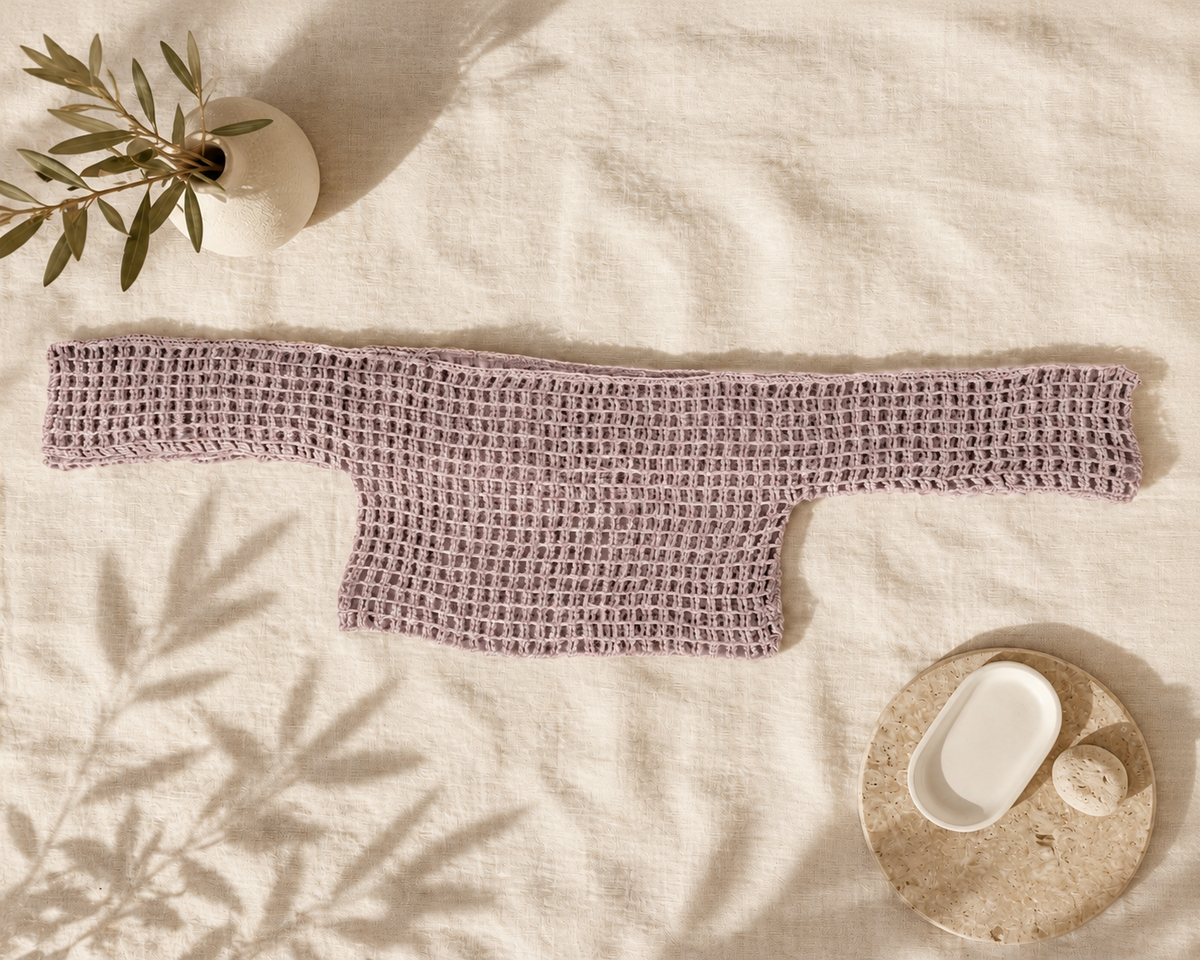 Dusty mauve long-sleeve crochet crop top laid flat with both sleeves extended on a light textile background.