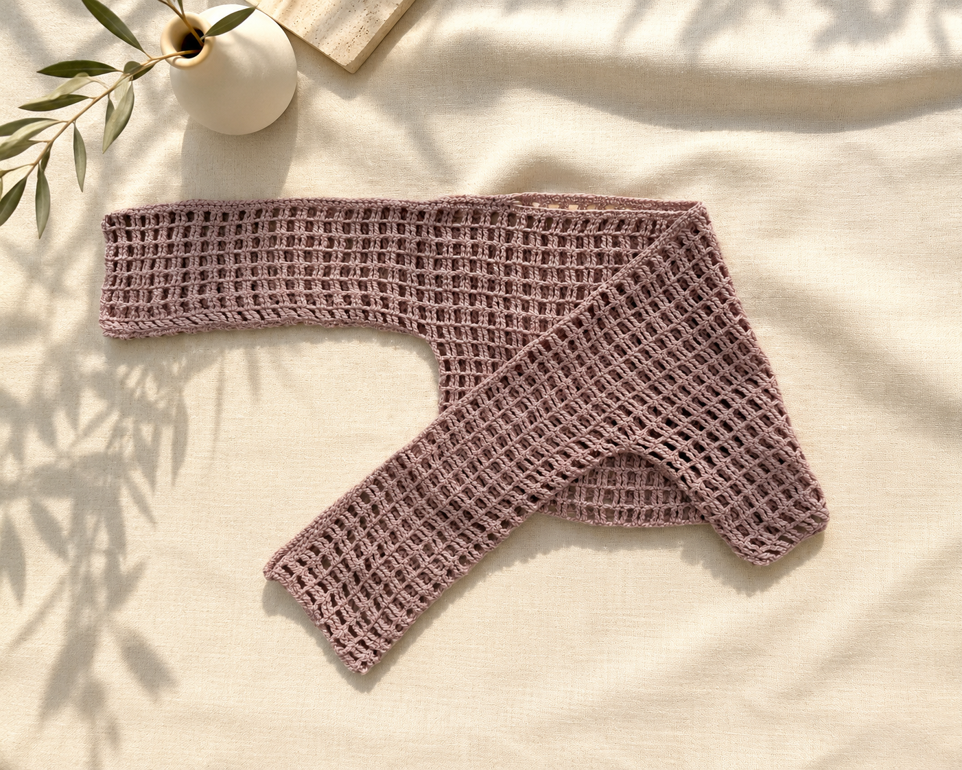 Handmade dusty mauve crochet crop top arranged diagonally to show its long sleeves, wide neckline and openwork construction.