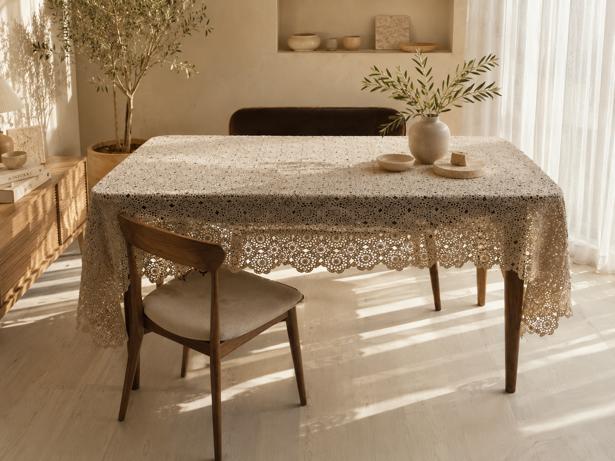 Handmade ecru crochet tablecloth styled on a dining table in a softly lit neutral interior.