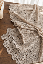 Close view of the handmade crochet tablecloth draped across a wooden surface, showing its openwork motifs and decorative edge.