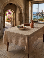 Handmade ecru crochet tablecloth displayed on a dining table in a rustic stone interior with natural light.