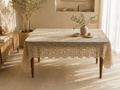 Large handmade ecru crochet tablecloth displayed on a rectangular dining table, showing its floral motif surface and draped edges.
