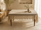 Large handmade ecru crochet tablecloth displayed on a rectangular dining table, showing its floral motif surface and draped edges.