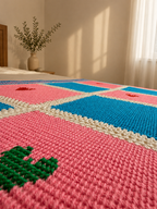 Close-up of a hand-embroidered green heart on a pink Tunisian crochet panel beside turquoise and cream sections.