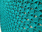 Close-up of the emerald green crochet top showing the lustrous microfibre acrylic yarn and repeating openwork stitch texture.