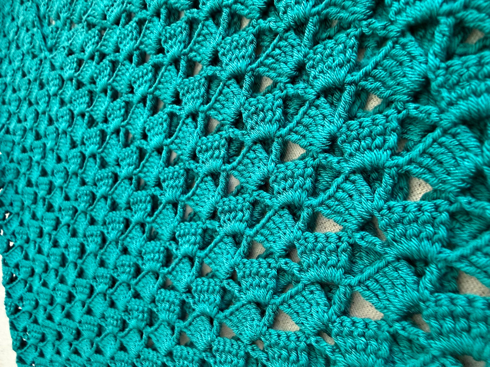 Close-up of the emerald green crochet top showing the lustrous microfibre acrylic yarn and repeating openwork stitch texture.