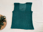 Full flat-lay view of the handmade emerald green crochet top showing its sleeveless shape, longline body and widening hem.