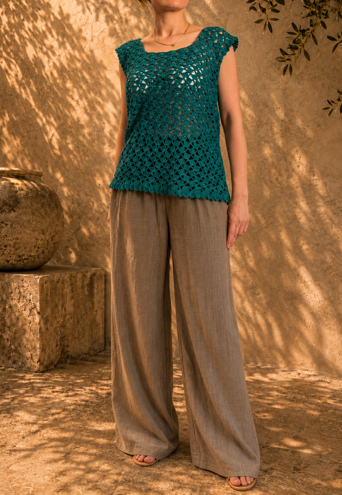 Front view of the handmade emerald green crochet top styled with natural wide-leg trousers, showing its scoop neckline and longline silhouette.