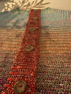 Close-up of the cardigan’s upper body, layered five-thread colour texture and contrasting hand-crocheted button placket.