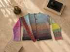 Editorial flat-lay of the open multicolour crochet cardigan showing the front panels, sleeves and gradient composition.