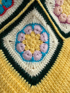 Macro view of one floral crochet motif showing its layered blue, lilac, yellow, cream and dark green colour sections.