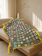 Large handmade floral motif crochet blanket styled over a neutral daybed as a colourful home textile layer.