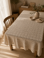 Angled view of the ecru crochet tablecloth arranged across a wooden dining table with its floral motifs clearly visible.