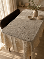 Large ecru floral motif crochet tablecloth styled on a dark wooden dining table in a warm interior.