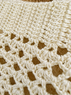 Close-up of the decorative openwork crochet pattern along the hem of the ivory tank top.