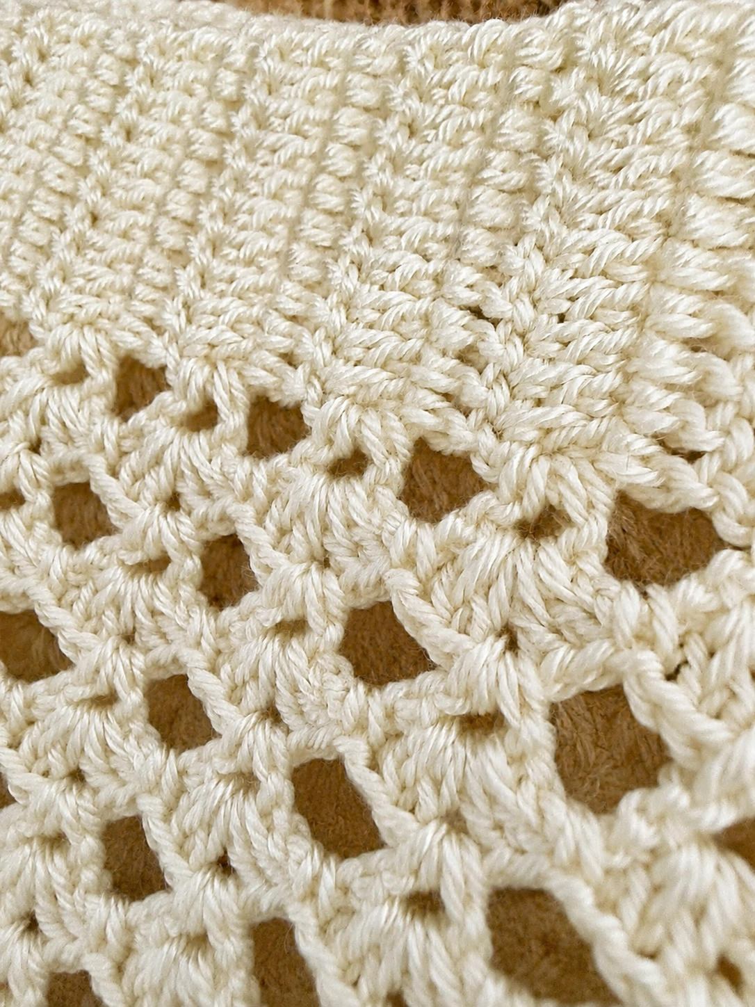 Close-up of the decorative openwork crochet pattern along the hem of the ivory tank top.