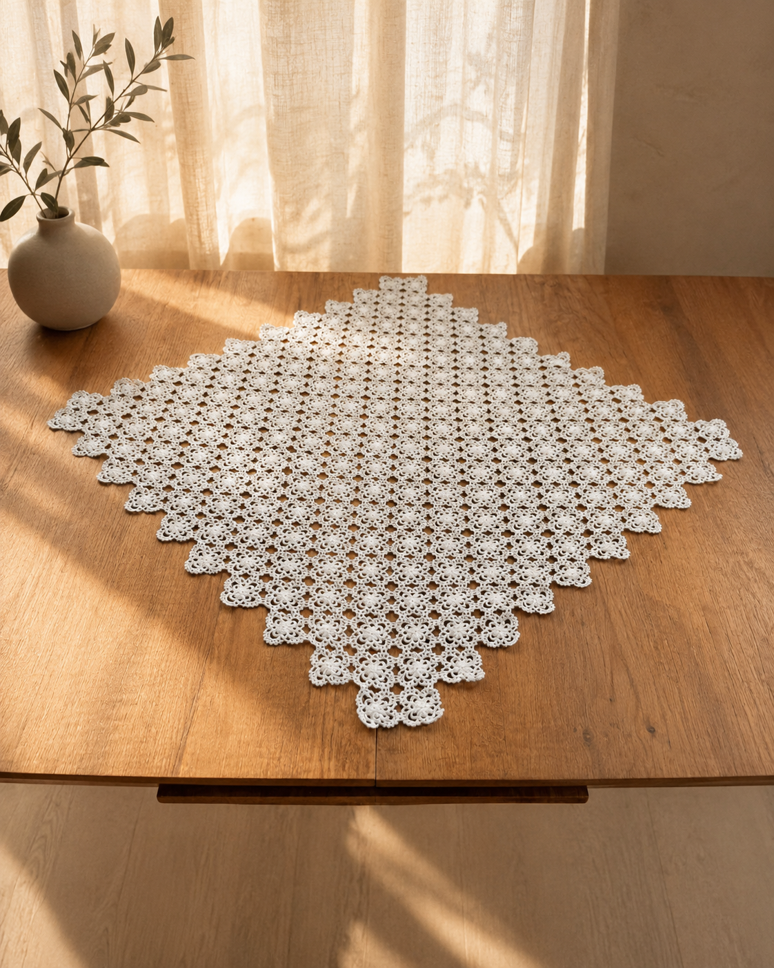 Large square white crochet table topper from a handmade cotton table-linen set, displayed on a wooden table.