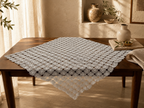 Large square white crochet table topper displayed on a wooden table, showing its expansive motif-grid construction.
