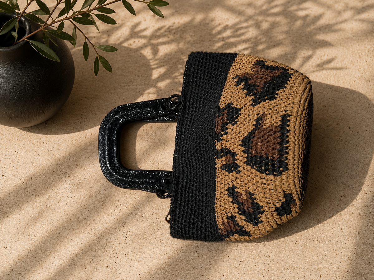 Side detail of the handmade paper yarn handbag showing the leopard-inspired crochet pattern and rigid glossy black handle.