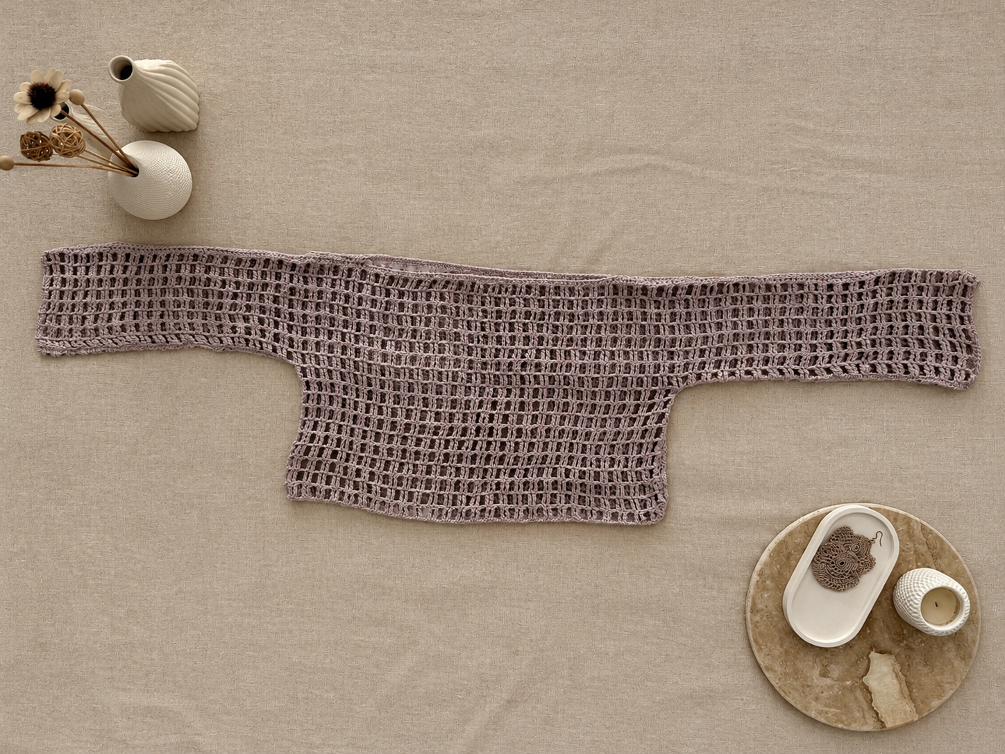 Full flat-lay view of the long-sleeve crochet crop top showing its cropped body, extended sleeves and relaxed proportions.