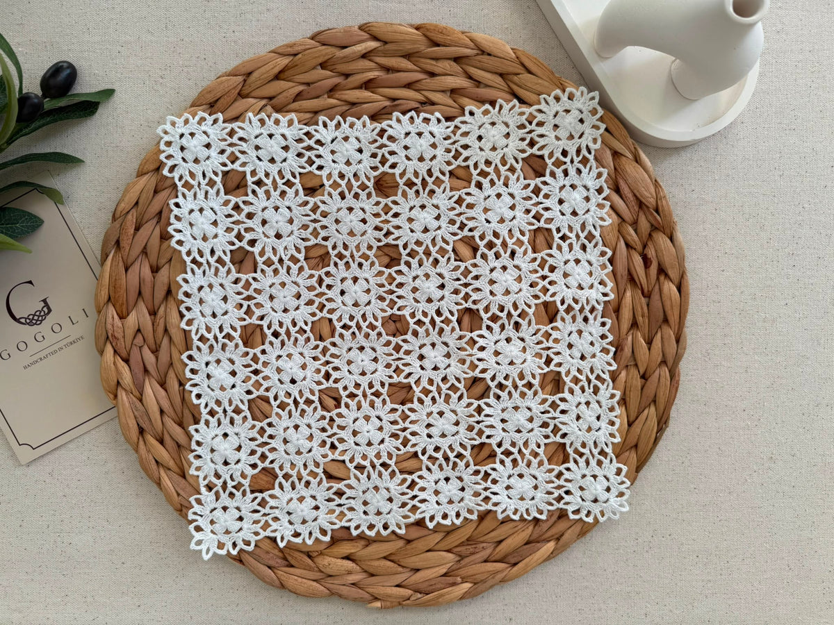 Medium square white crochet doily displayed on a woven surface, showing its larger coordinated motif arrangement.
