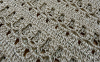 Macro view of the taupe-grey crochet fabric showing the fine metallic fibres and softly shimmering yarn surface.