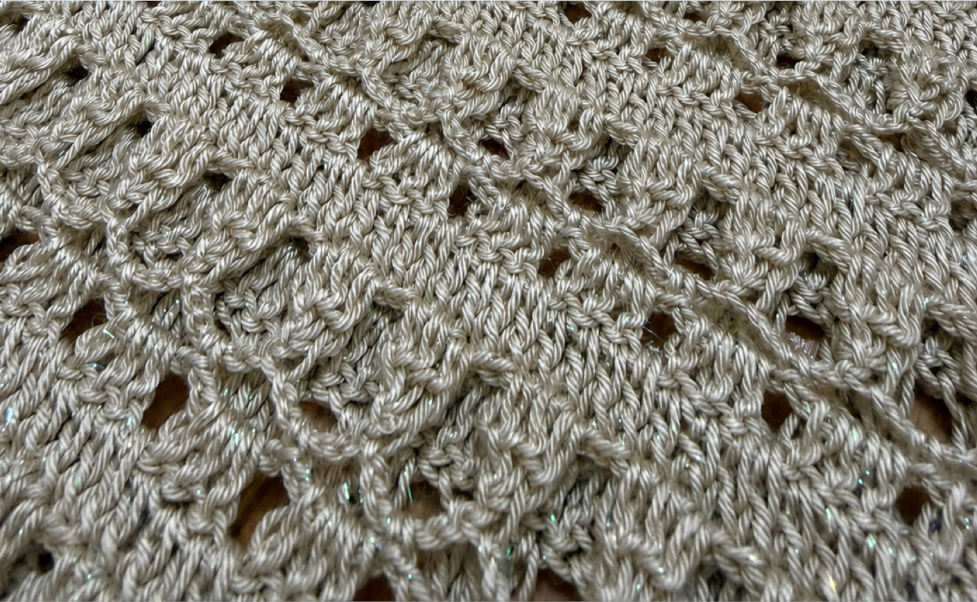 Macro view of the taupe-grey crochet fabric showing the fine metallic fibres and softly shimmering yarn surface.