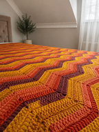 Close view of the multicolour chevron blanket draped across a bed, showing its soft texture and flowing pattern.