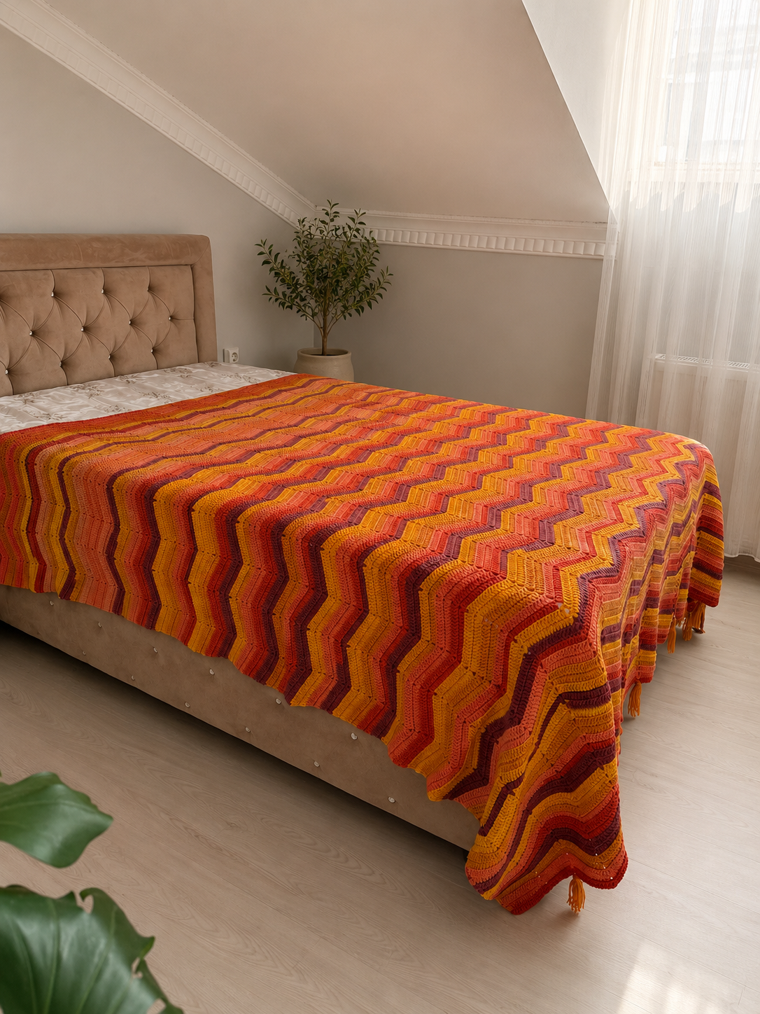Angled view of the large chevron crochet blanket draped naturally over the side and foot of a bed.