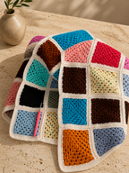 Folded multicolour crochet blanket showing its substantial drape, square motifs and cream border.