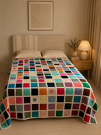 Handmade multicolour crochet motif blanket displayed across a bed, shown from the front.