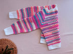 Folded view of the multicolour crochet cardigan showing the striped sleeves, contrasting white cuffs and handmade stitch texture.