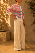 Side view of the handmade multicolour crochet cardigan styled with ivory wide-leg trousers, showing its striped sleeves and contrasting white trims.