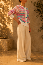 Side view of the handmade multicolour crochet cardigan styled with ivory wide-leg trousers, showing its striped sleeves and contrasting white trims.