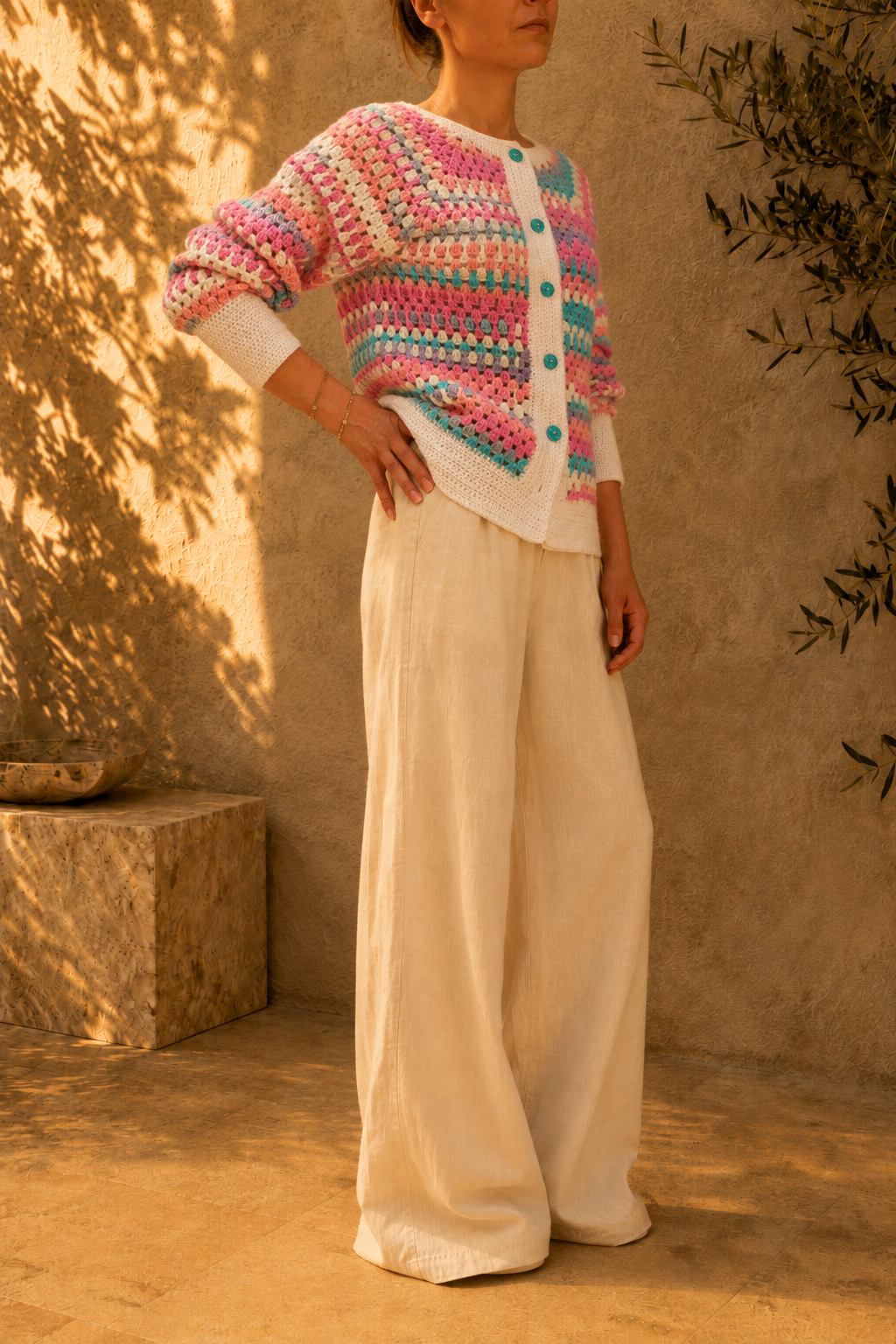 Side view of the handmade multicolour crochet cardigan styled with ivory wide-leg trousers, showing its striped sleeves and contrasting white trims.